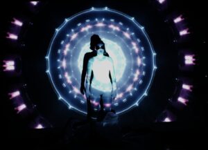 Uma pessoa está em pé na frente de uma projeção de luz vibrante e simétrica com tons de azul e roxo, usando óculos escuros e uma roupa de cor clara. O design de fundo lembra um padrão de caleidoscópio, adicionando um efeito dramático. Foto: @mylenamaciels