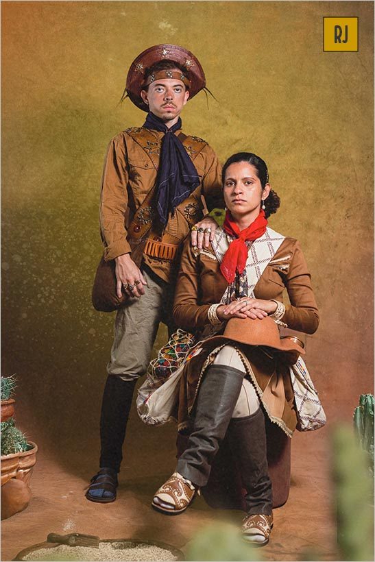 A foto é um retrato de um casal de cangaceiros. A mulher está sentada em um toco enquanto um homem, está de pé atrás dela. Em torno deles, vasos com cactus. Foto: Paulo Aragon