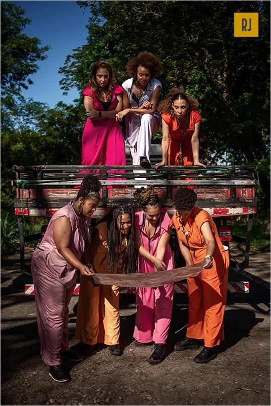 A foto mostra sete mulheres. três delas estão em cima da caçamba de um caminhão e olhma para um mapa que es†a sendo seguro pelas outras quatro mulheres que estão no chão, abaixo das primeiras e também olham o mapa. No fundo, muitas árvores. Foto: Ira Barillo